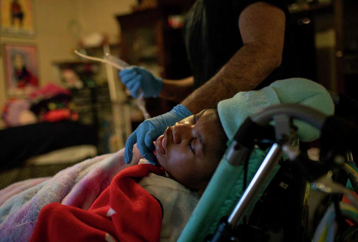 Hailey Cheevers, 10, sits in a chair in her living room as Samir Haq, a home-health nurse, prepares to do endotracheal suctioning after she returned home following several days of winter storms Friday, Feb. 19, 2021, at her home in Houston.