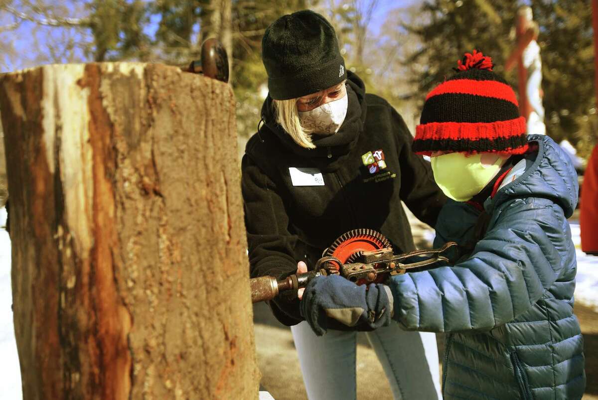 Farm and environmental educator Debby Ritchie assists Dylan Tobin, 6, of Greenwich, using a hand drill to tap a maple tree.