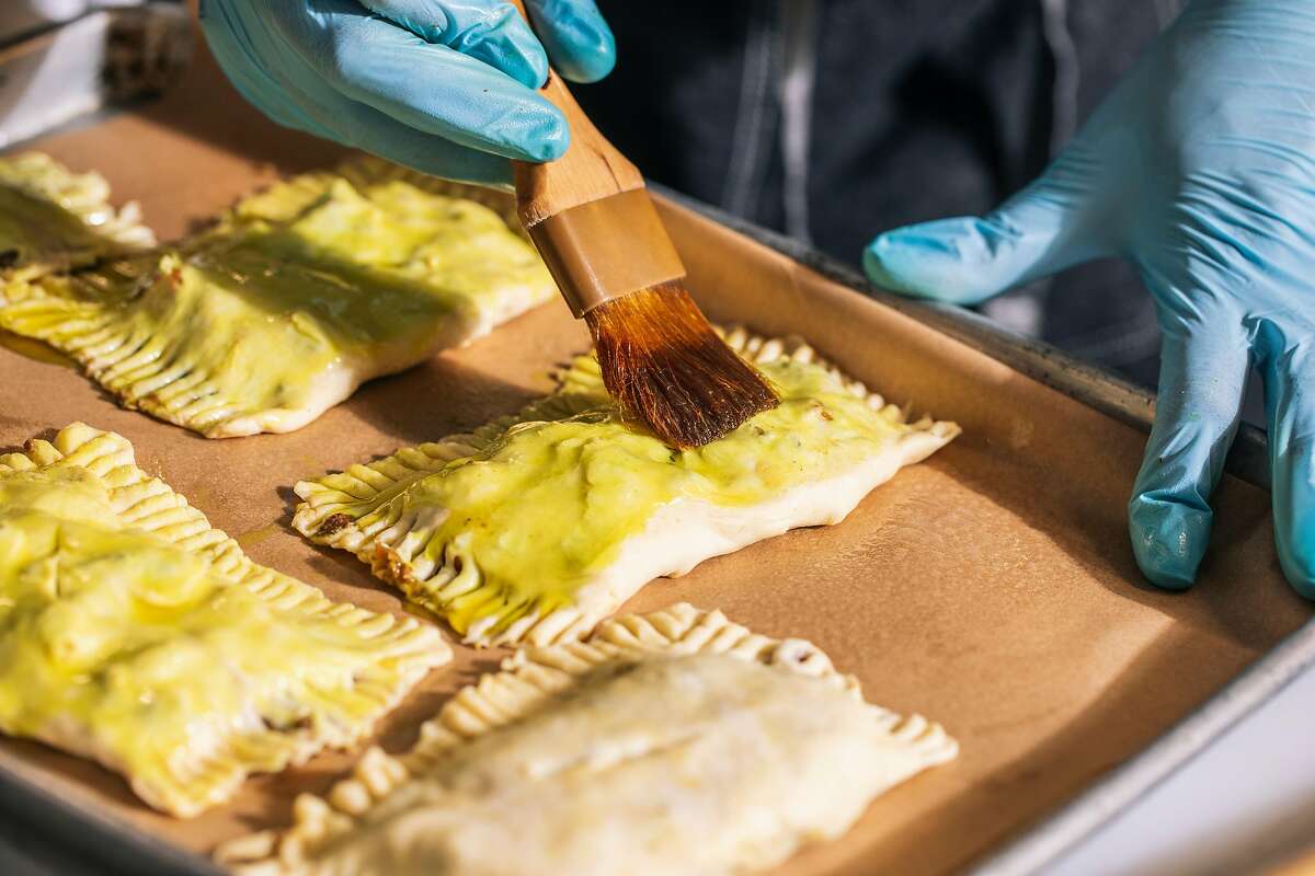 Chef Christina Wilson, owner of The Pleasure Principle Dining Events, brushes curry oil onto a tray full of Jamaican beef patties at a shared kitchen in Oakland, Calif. on Tuesday, Feb. 9, 2021.