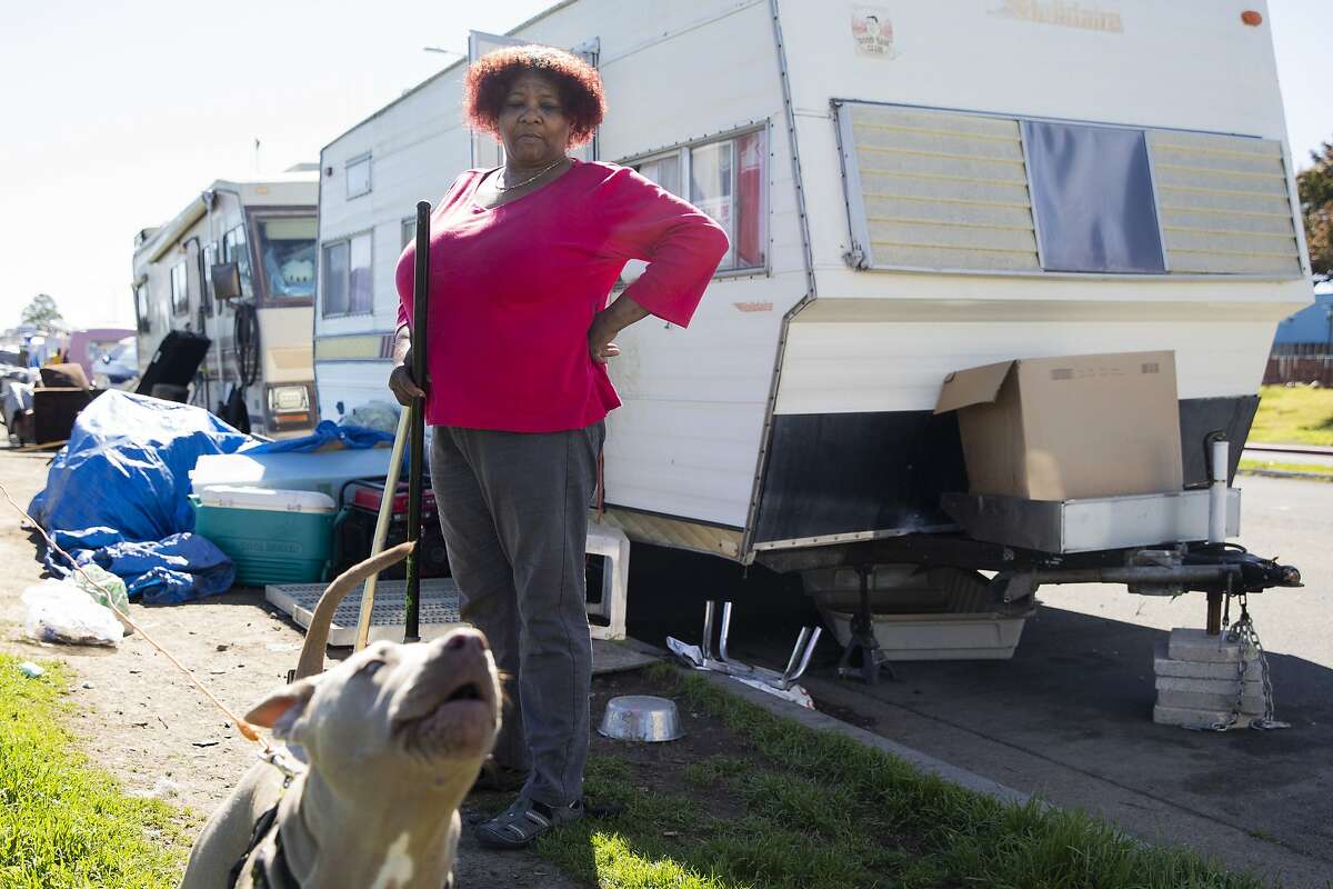 Amilee Smith cleans up the area outside of her RV with her dog Mimi while parked at an encampment along Rydin Road in Richmond.