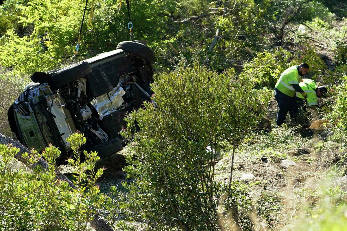 Workers remove debris near a vehicle on its side after a rollover accident involving golfer Tiger Woods Tuesday, Feb. 23, 2021, in Rancho Palos Verdes, Calif., a suburb of Los Angeles. Woods suffered leg injuries in the one-car accident and was undergoing surgery, authorities and his manager said.