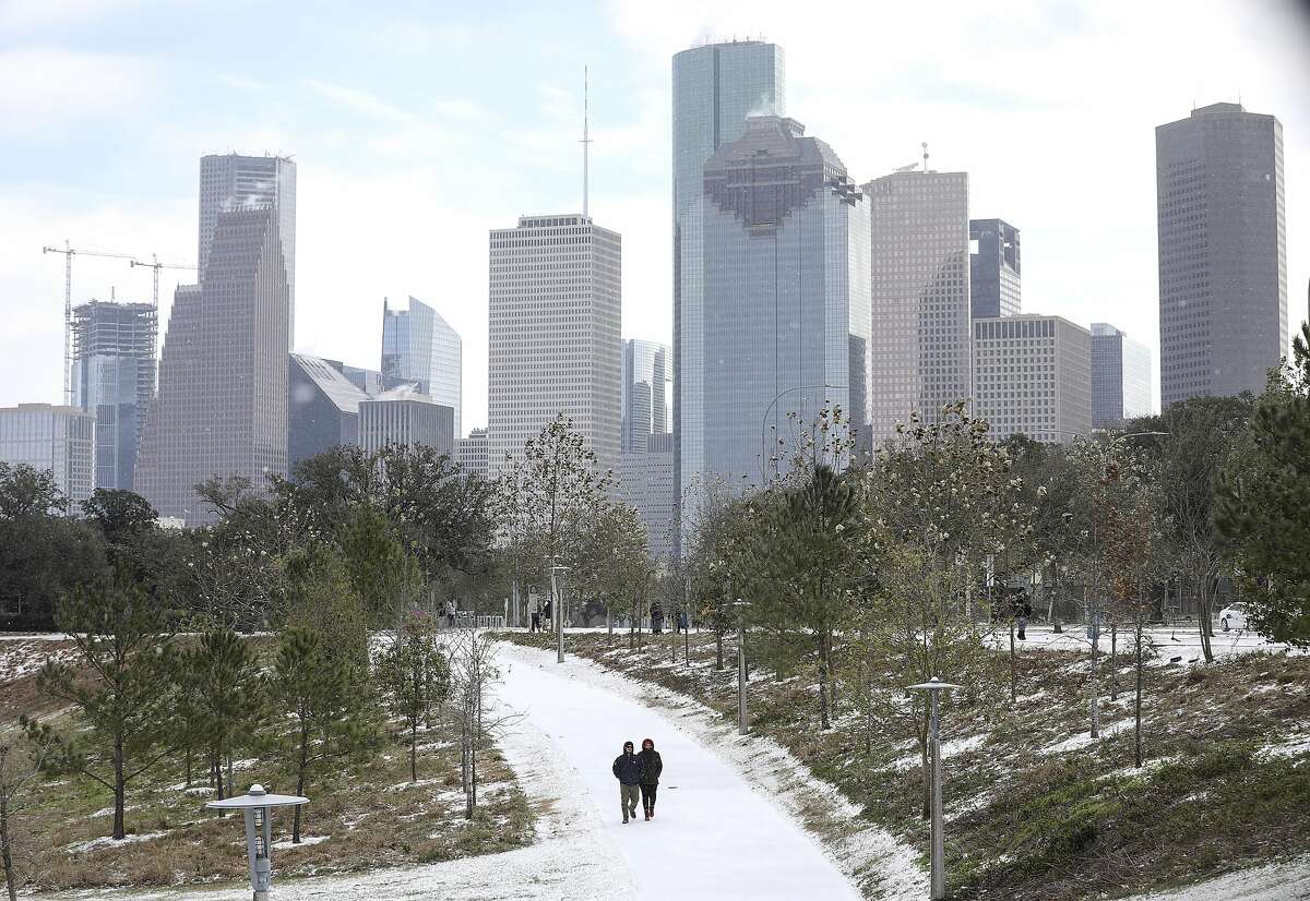 Two people walk through snow as a winter storm hits Houston on Monday, Feb. 15, 2021, at Buffalo Bayou Park in Houston.