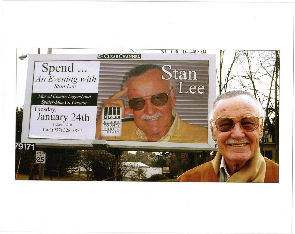 Stan Lee poses in front of a billboard promoting an upcoming appearance.