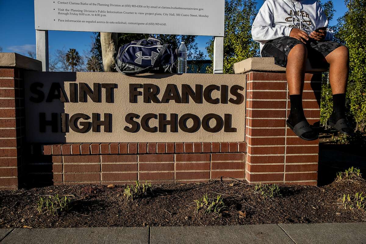 A student sits on a sign by the entrance to Higgins Field at St. Francis High School in Mountain View, California Wednesday, Feb. 17, 2021.