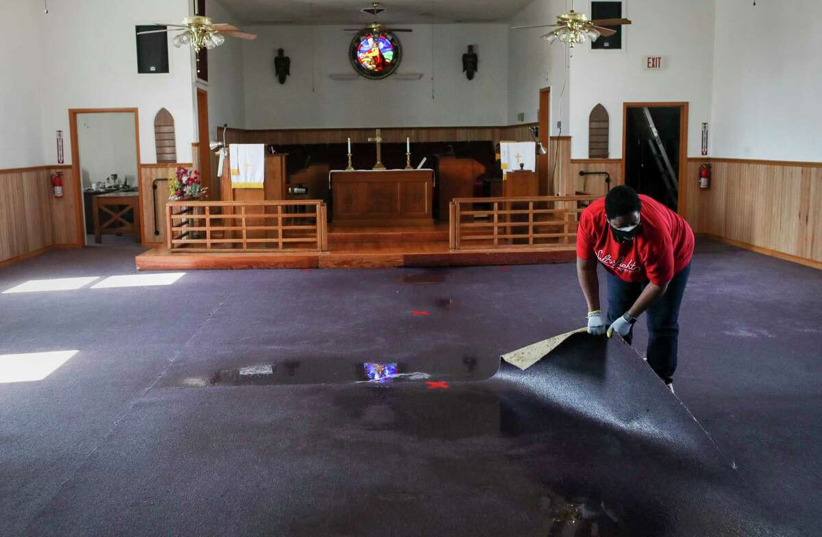 Pastor Enid Henderson rolls up wet carpet as she and others clean up water from a busted pipe Saturday, Feb. 20, 2021, at Ebenezer United Methodist Church in Houston.