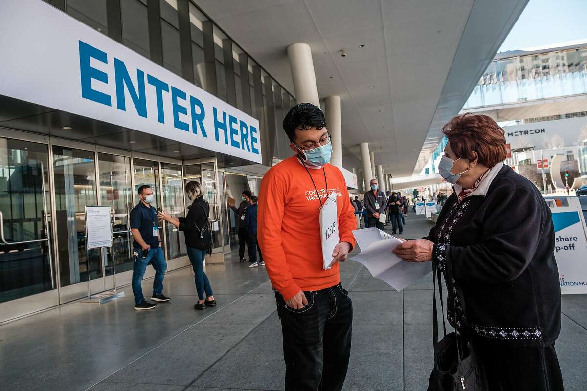 A greeter helps people arriving for vaccinations at San Francisco’s Moscone Center. The city is a leader in vaccinations.