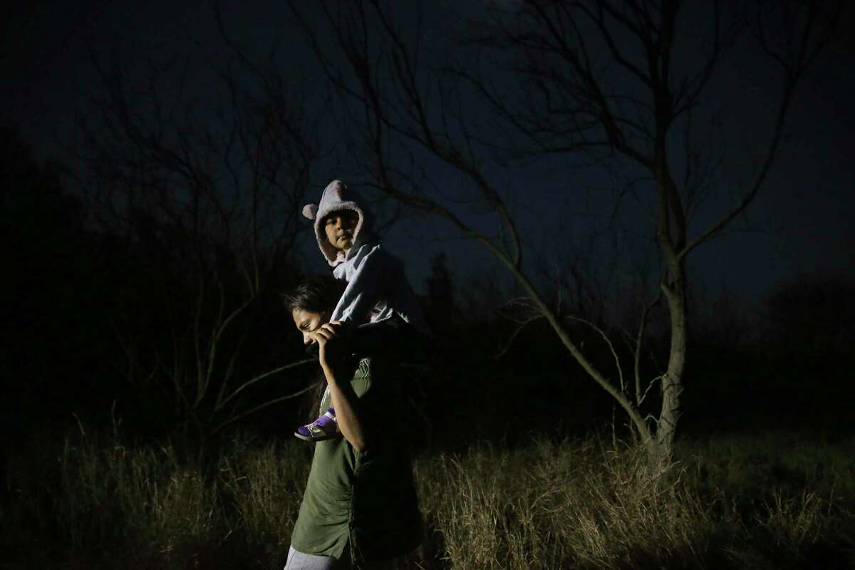 A migrant woman carries a child as they walk on a caliche road after crossing the Rio Grande into the U.S. at a placed called Rincon del Diablo, Devil’s Corner, in Hidalgo County, Texas, Wednesday, Feb. 24, 2021. Over two hundred crossed a in short time at the spot where families turn themselves into immigration authorities.