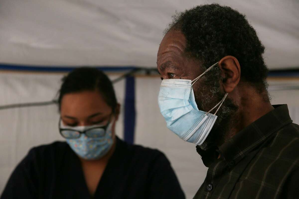 Richard Herron (right) wears a double mask while Laray Bonilla, paramedic intern City College of San Francisco, prepares a Moderna COVID-19 vaccine for him at the Southeast Health Center in San Francisco.