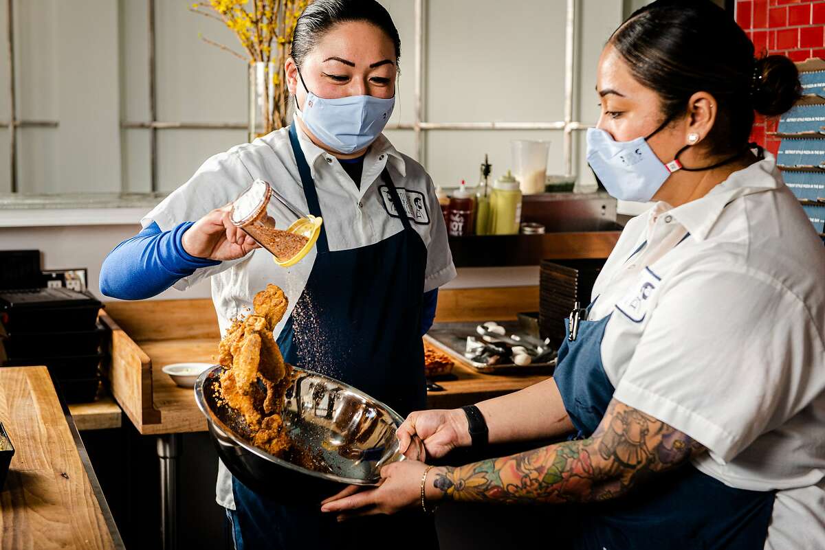 Square Pie Guys general managers Louise Tang (left) and Yahaira Santini toss chicken wings at the restaurant's new Oakland location.