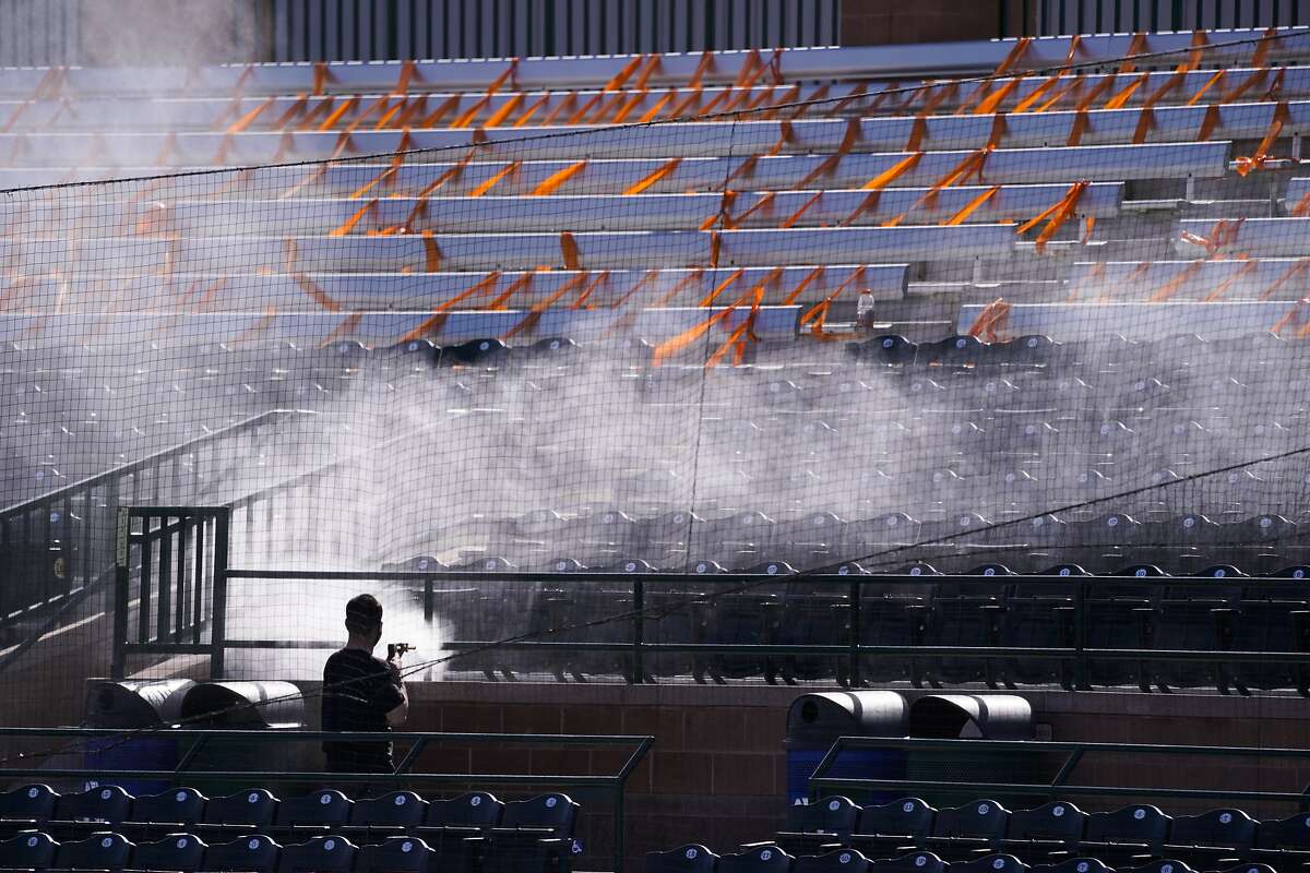 A worker cleans seats taped off for social distancing ahead of Sunday's baseball game between the San Francisco Giants and the Los Angeles Angels at Scottsdale Stadium in Arizona.