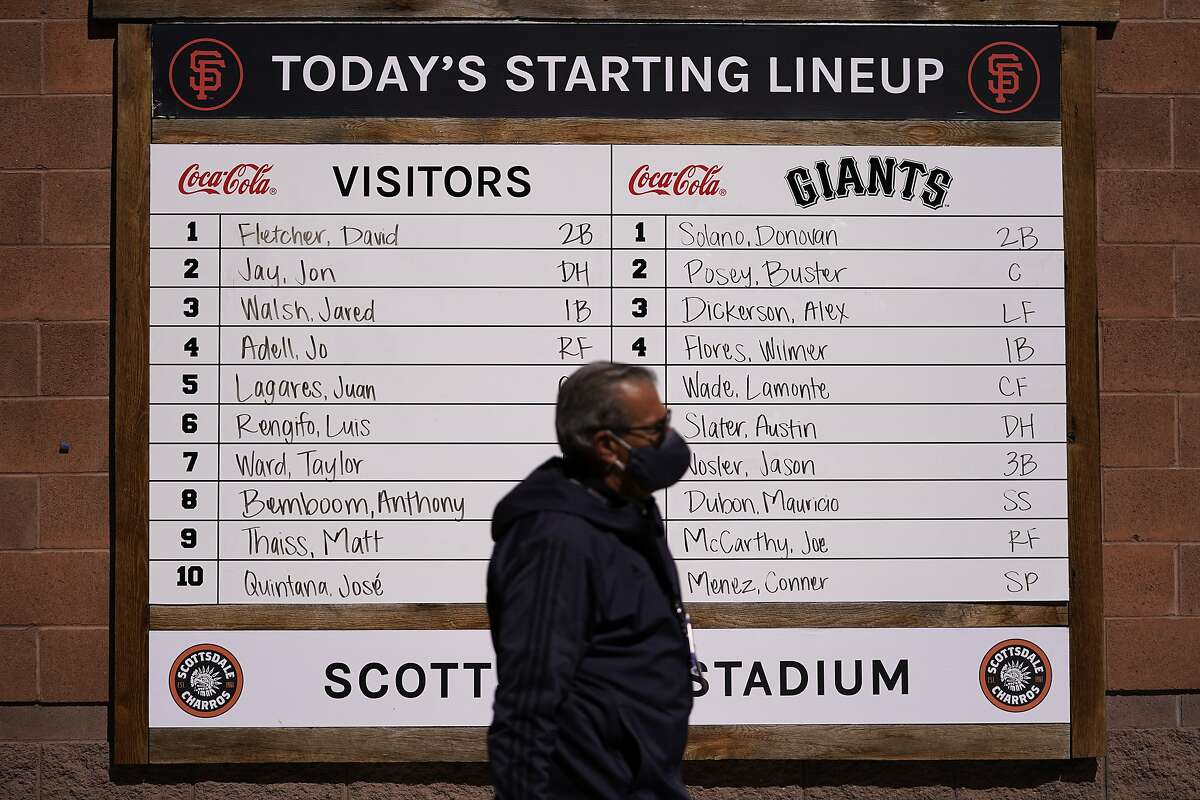 A man with a face mask walks past a lineup board before a spring baseball between the San Francisco Giants and the Los Angeles Angels in Scottsdale , Ariz., Sunday, Feb. 28, 2021. (AP Photo/Jae C. Hong)