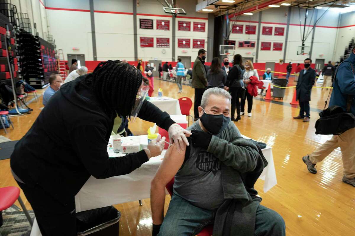 Registered Nurse Stephenie Champion, left, vaccinates Ramon Soto, 65, on Feb. 10, at Central High School in Bridgeport. The mass vaccination clinic is one of several ways Bridgeport officials are trying to fight the low vaccination rates many cities across the country are seeing compared with wealthier suburbs.