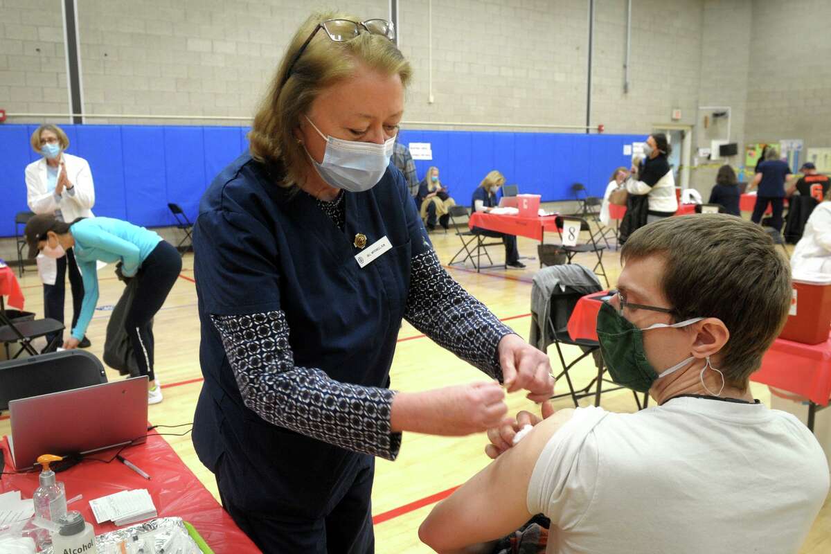 Jill Mitchell, the head nurse administrator for the Town of Fairfield, places a band aid on the arm of David Kean, a music teacher from Rochambeau Middle School, in Southbury, following his COVID-19 vaccination at the Bigelow Center clinic in Fairfield on Monday.