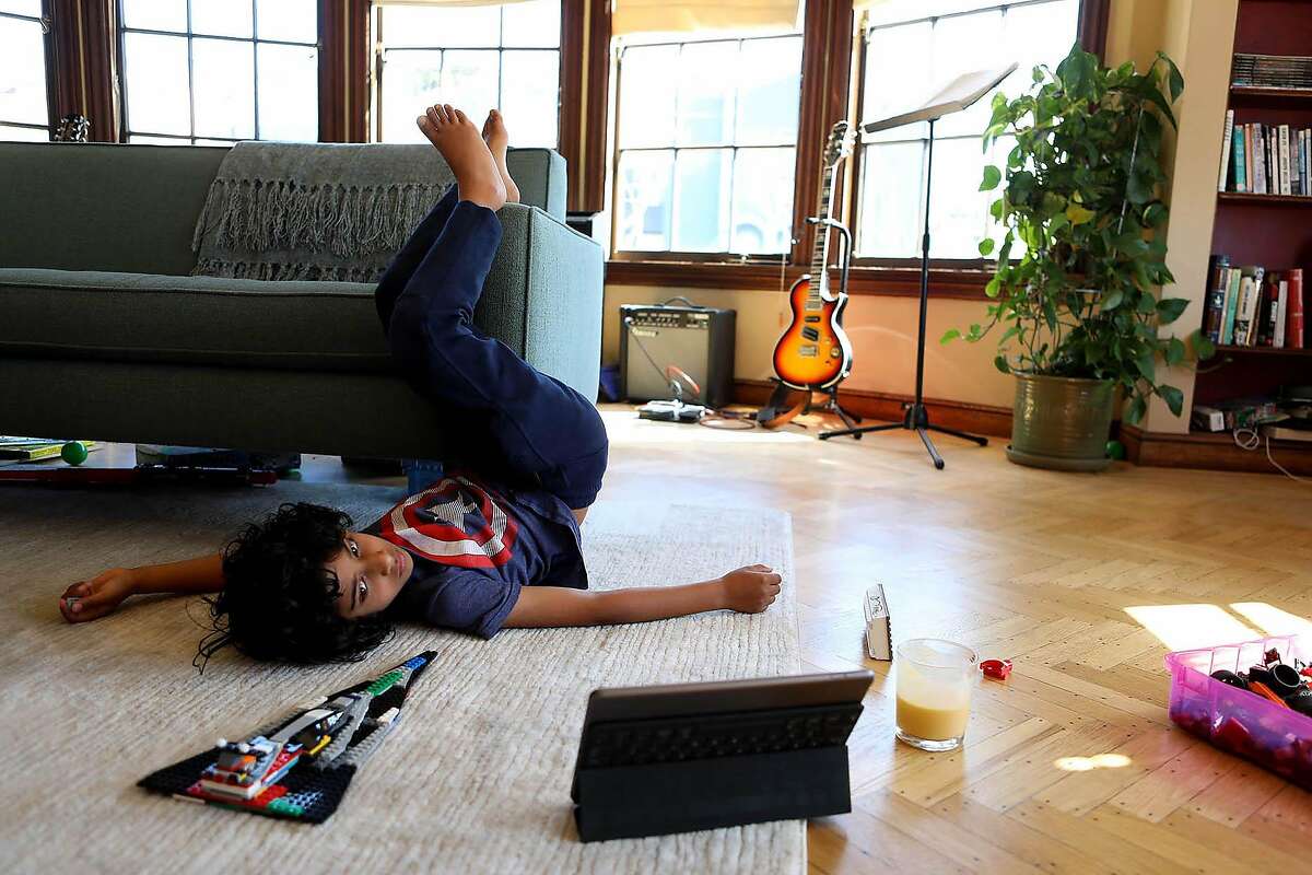 Jeevan Guha, 6, relaxes on the living room floor as he attends his West Portal Elementary Zoom first-grade class.