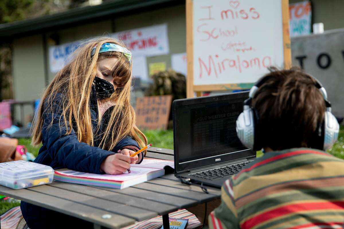 Miraloma 1st grader Colette Schwab, 6, and Thomas Zinnis, 1st grader at Clarendon, 6, work on homework and attend class on their computers at Midtown Terrace Park in San Francisco, February 18, 2021 to participate in a demonstration with fellow students for reopening.