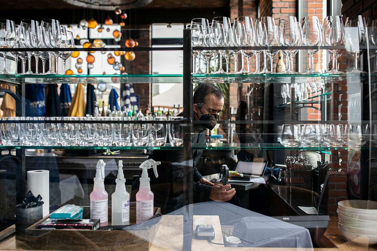 Ricardo Torres, assistant general manager at Waterbar in San Francisco, tidies up the bar. San Francisco is making new adjustments that ease pandemic restrictions for bars, restaurants and other activities.