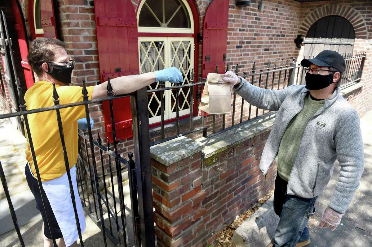 Fourth generation owner of Louis' Lunch Jeff Lassen hands parking lot attendant and regular customer Rey Colon his lunch over a fence next to the hamburger joint in New Haven on May 13, 2020. The fast-food restaurant is open for take-out but is closed for dining inside due to the COVID-19 epidemic.
