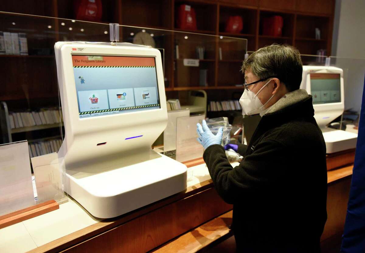 Circulation, Cataloging, and Aquisitions Supervisor Alex Lee refills the plastic finger protectors from the self check-out counter at Fergsuon Library in Stamford, Conn. Thursday, Feb. 4, 2021. Outside agencies got a cash infusion from the city's planning board in this year's budget recommendation, and the Ferguson Library was one of the organizations to reap the benefit.