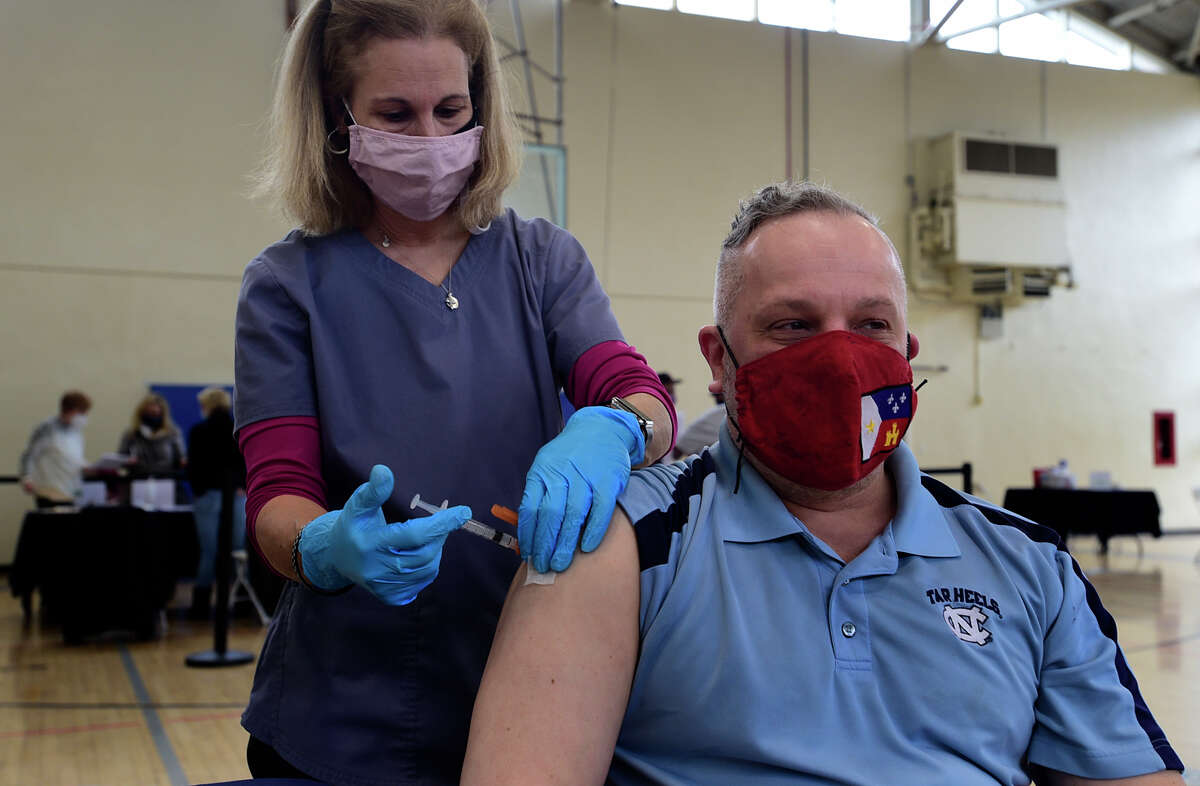 Tokeneke scool nurse Kim Martini administers the shot to Darien High School french teacher Bruce Mitchell as teachers get vaccinated against the coronavirus Saturday, March 6, 2021, at Town Hall in Darien, Conn.