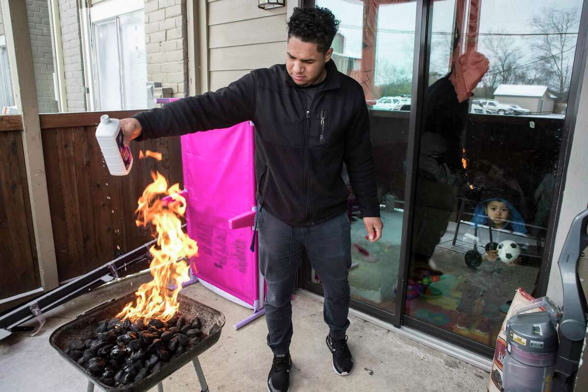 Kevin Morazan lights his charcoal grill to cook after losing power in the Greenspoint area due to rolling blackouts following an overnight snowfall Monday, Feb. 15, 2021 in Houston. Temperatures plunged into the teens Monday with light snow and freezing rain. The stove in his apartment is electric.