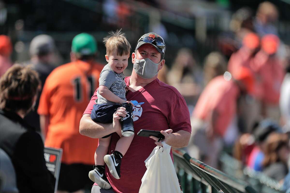 A fan carries his son through the concourse after stopping for refreshements as the San Francisco Giants played the Chicago White Sox in a spring training game at Scottsdale Stadium in Scottsdale, Ariz., on Thursday, March 4, 2021.