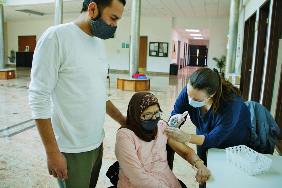 Ali Haroon, left, stands by his mom, Amina Haroon, as she eceives her first dose of the Moderna Covid-19 vaccination, given by Laura Ordway, the public health pharmacist at The Collaboratory, Albany College of Pharmacy and Health Sciences. The Albany College of Pharmacy and Health Sciences held at vaccination clinic at the Al-Hidaya Center for people 65 years of age or older on Tuesday, March 9, 2021, in Latham, N.Y.  (Paul Buckowski/Times Union)