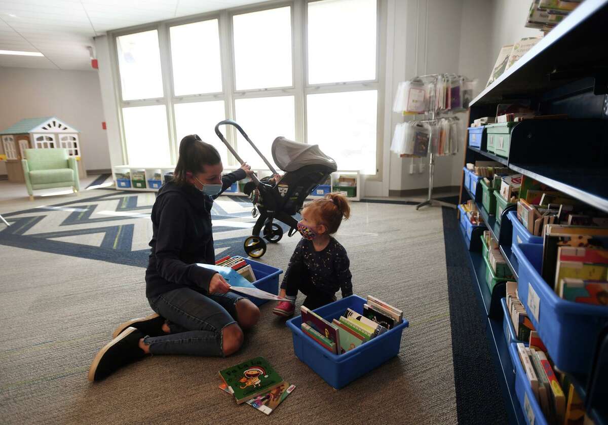 Caitlyn Brion, of Milford, picks out books with her daughter Ruby, 2, during the opening day of the newly remodeled children's library.