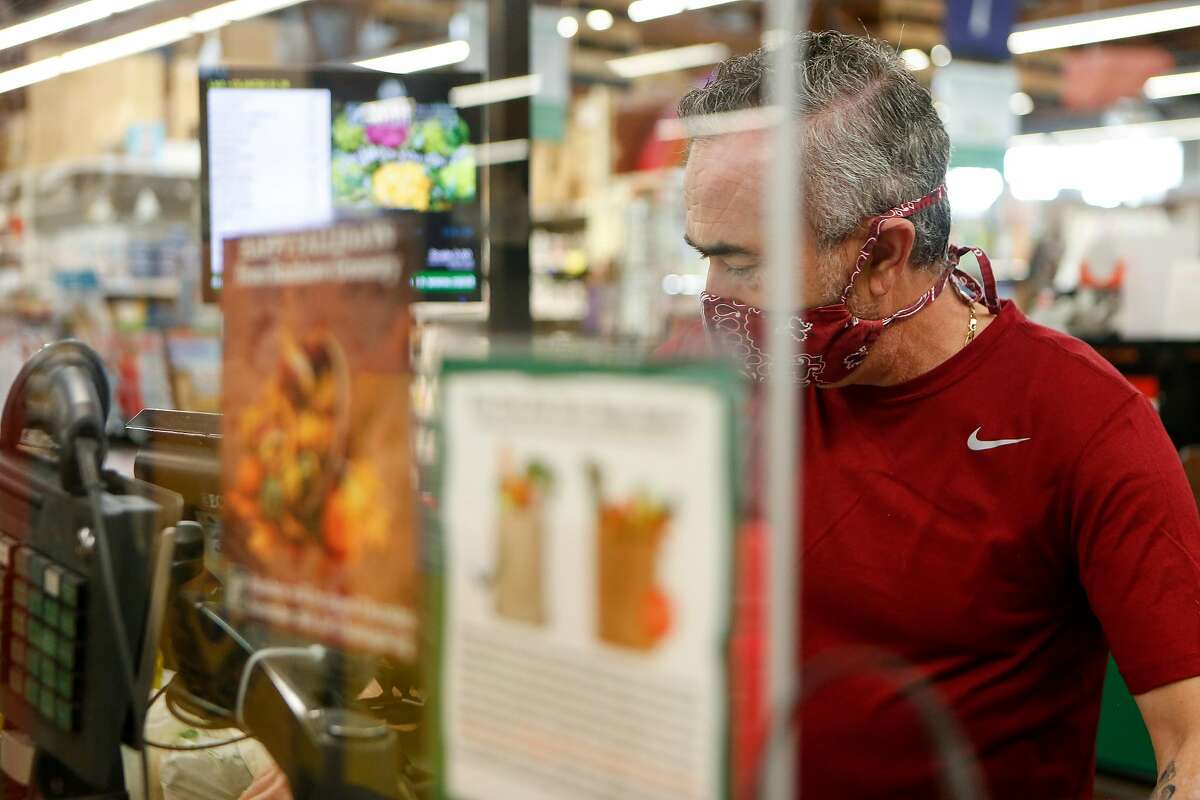 Juan Salazar checks out a customer from behind plexiglass at Rainbow Grocery in November in San Francisco.