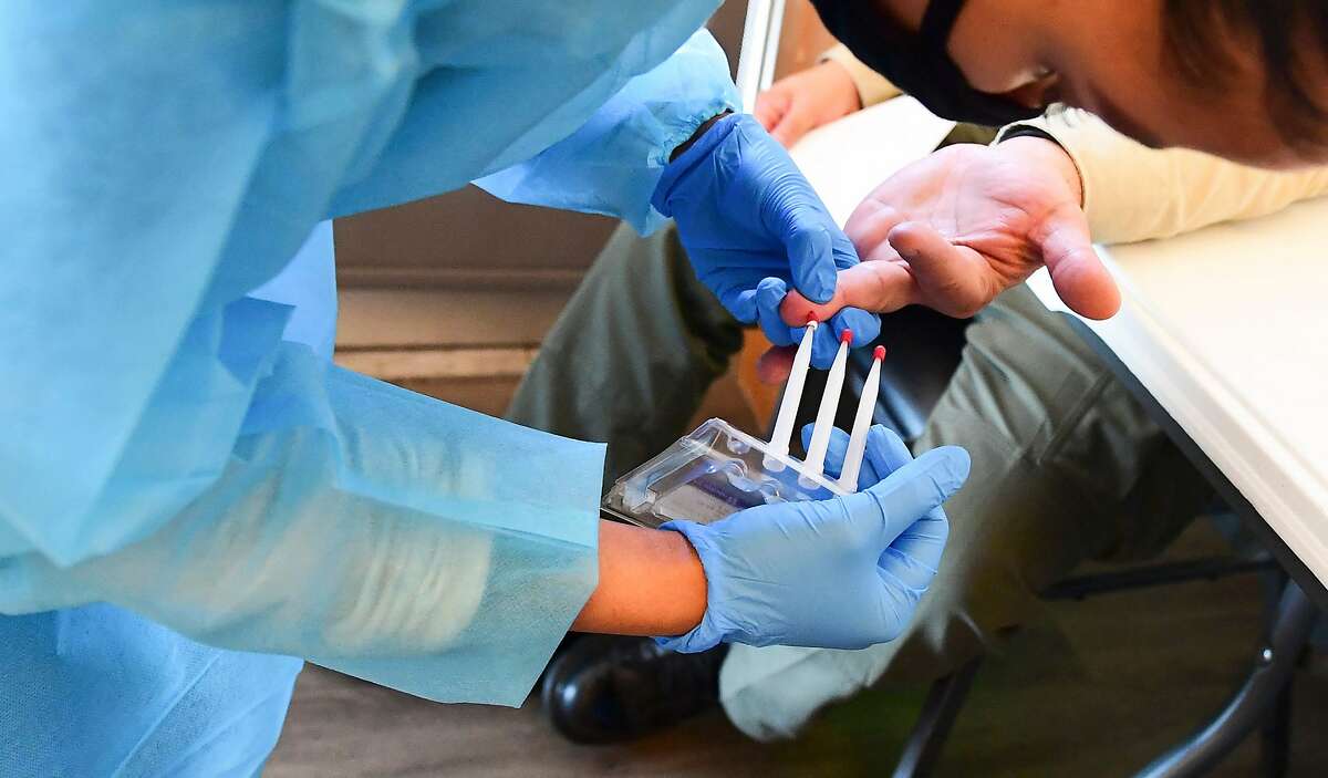 A phlebotomist takes blood through a finger prick during a no-cost COVID-19 antibody testing organized by the GuardHeart Foundation and the city of Pico Rivera, Los Angeles County.