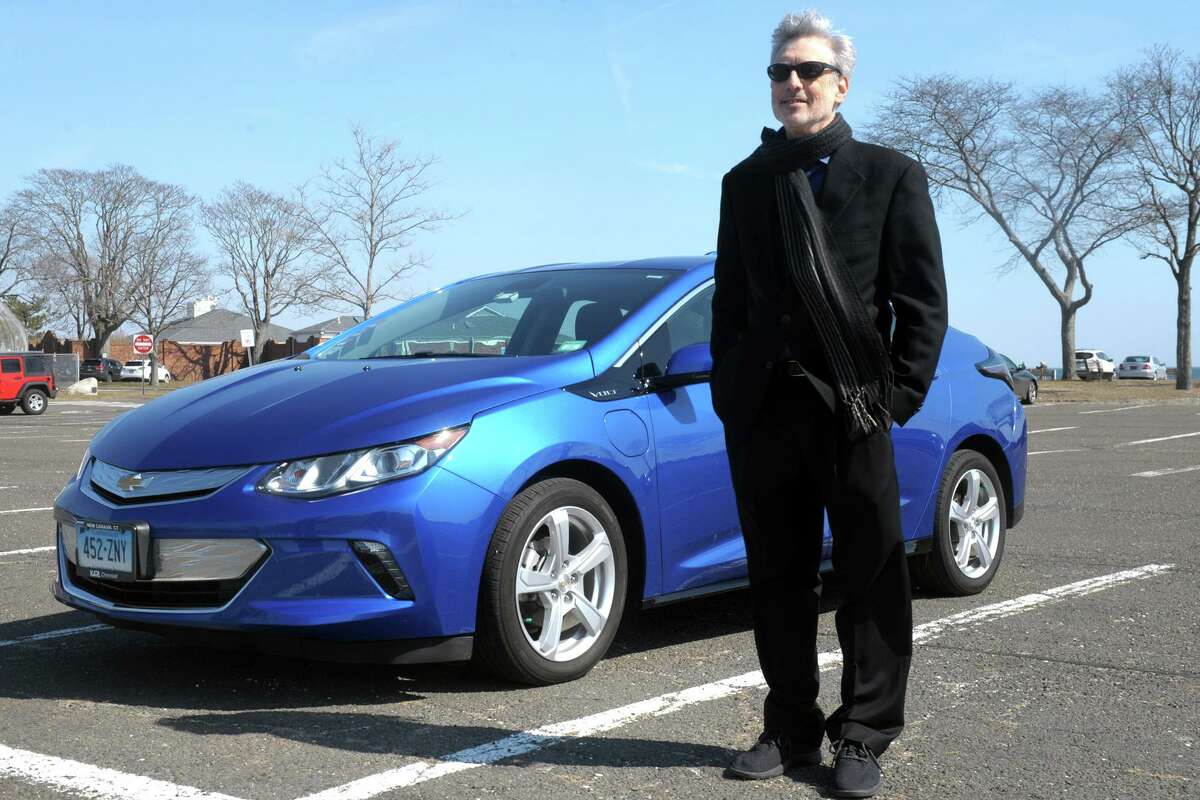Barry Kresch, president of the EV Club of Connecticut, stands next to his 2016 Chevy Volt, at Compo Beach in Westport, Conn., on March 9, 2021. Kresch purchased the vehicle in 2015 with a rebate through the state’s Connecticut Hydrogen Electric Automobile Purchase Rebate (CHEAPR) program.