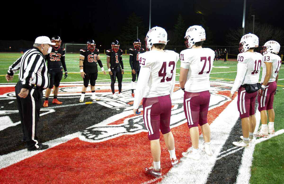 Due to continuing COVID-19 protocols, team captains from Aragon High School, left, and visiting Sacred Heart Prep maintain a healthy distance for the coin toss before a high school football game on Friday.