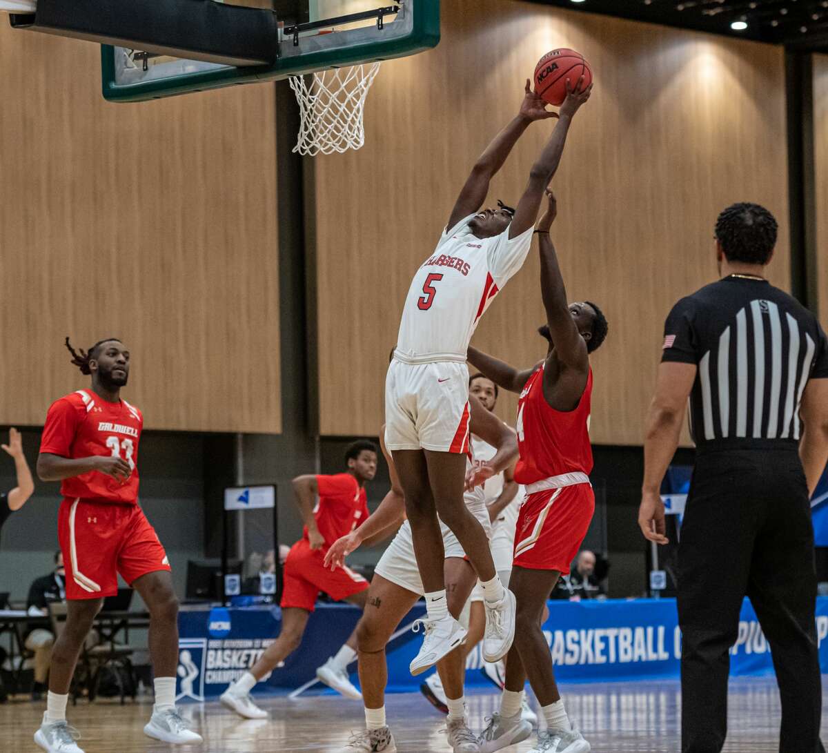 Dominican's Jalen Burgess skies for a rebound between Caldwell defenders Gerald Blount (33) and Manley Dorme in a NCAA Division II basketball regional game Saturday, March 13, 2021, at the Albany Capital Center. (Robert Simmons/ACC)