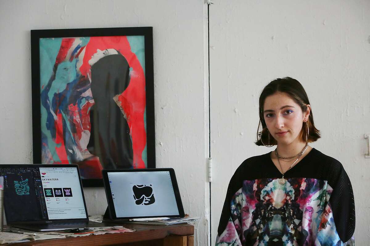 Mixed media artist Göksu Ilgaz Koçakcigill, also known as @skywaterr, stands for a portrait next to works of her digital art displayed on her laptop and tablet in her studio on Friday, March 12, 2021 in San Francisco, Calif.