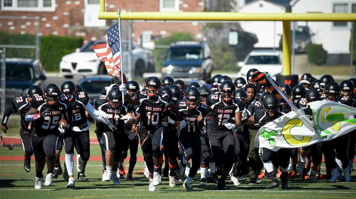 Stamford's Danny Simms (10) carries the flag as he leads the Blackknights charge onto the field prior to the kick off against Trinity Catholic/Wright Tech at Boyle Stadium on Oct. 5, 2019.