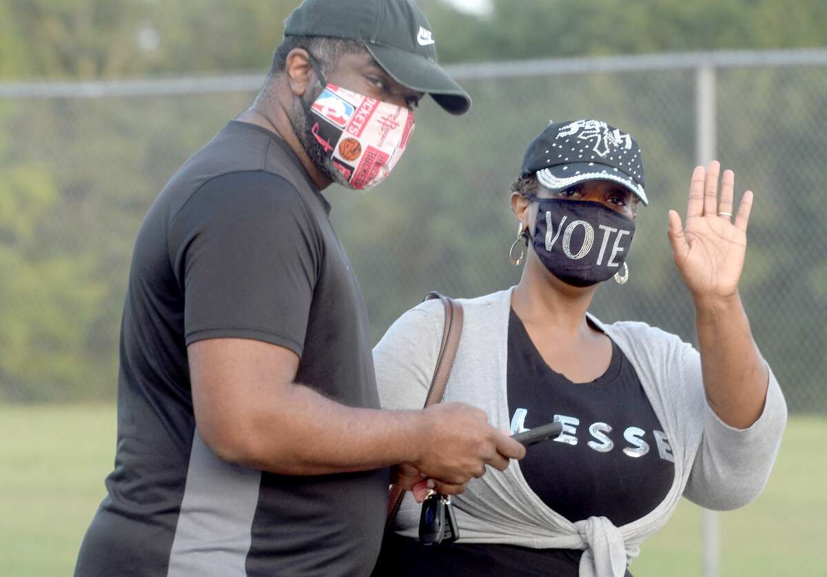 Yolanda Wells waves, wearing her bedazzled VOTE mask, as she and husband Wayne Wells wait in the long line that stretched along the drive at Rogers Park, extending onto Gladys Avenue, before polls opened at 8 a.m. for the first day of early voting in Texas. Photo taken Tuesday, October 13, 2020 Kim Brent/The Enterprise