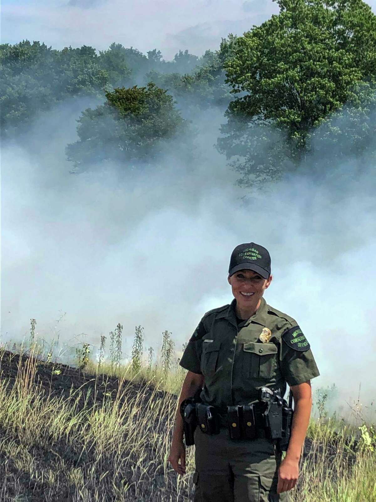 Michigan Conservation Officer Angela Greenway stands in front of smoke from an extinguished wildfire along US-131 that she responded to in 2019. (Courtesy photo/Michigan Department of Natural Resources)