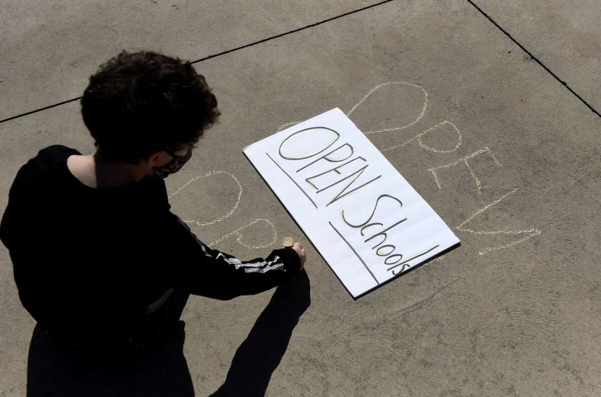 Alexander Eldridge, a kindergarten student from Schenectady, writes a chalk message in West Capitol Park urging lawmakers to change social distancing rules to conform with new CDC guidance so schools can reopen on Monday, March 22, 2021, in Albany, N.Y. His mother, Miranda, says that the 45 minutes of in-person schooling per day he currently receives is not enough for him. (Will Waldron/Times Union)