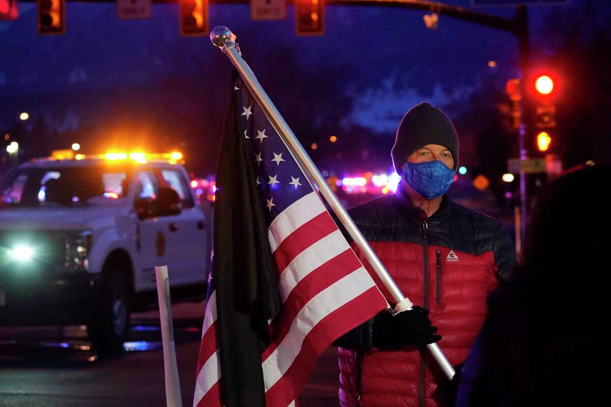 A man holds an American flag as a procession of emergency vehicles leaves a King Soopers grocery store where a shooting took place Monday, March 22, 2021, in Boulder, Colo.