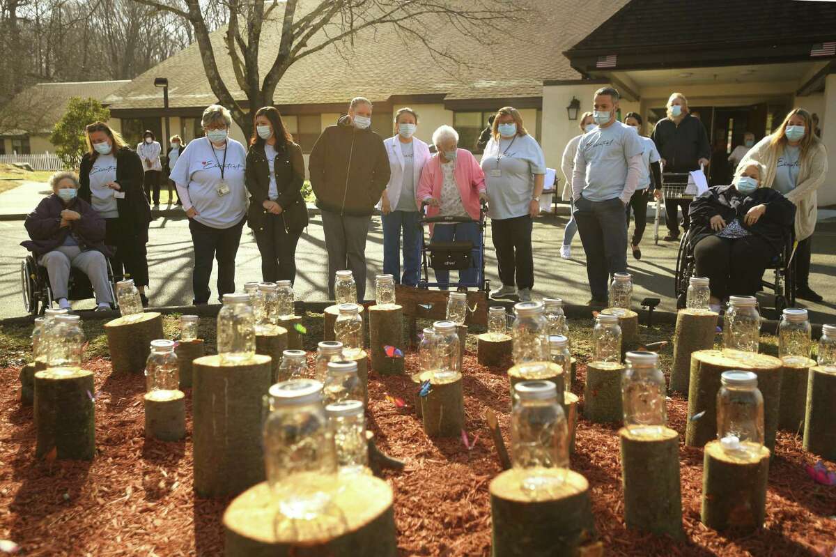 Staff and residents view the memorial in honor of the fifty residents to die since the start of the Covid-19 pandemic one year ago outside Apple Rehab Shelton Lakes in Shelton, Conn. on Tuesday, March 23, 2021. Nearly half of the deaths were due to Covid.