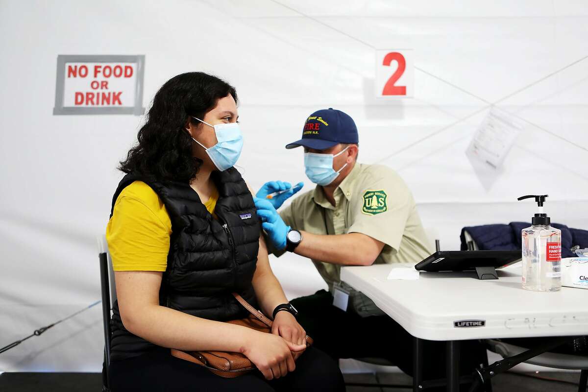 Jessica Avila, 23, of Berkeley, receives her second dose of the Pfizer vaccine as it's administered by Brandon Tatlow, of the U.S. Forest Service, Lassen National Forest, at the Oakland Coliseum vaccination site on Thursday, March 25, 2021, in Oakland, Calif. The Coliseum vaccination site is only scheduled to be open for eight weeks, which means it will close in three weeks unless a deal is reached with local officials.