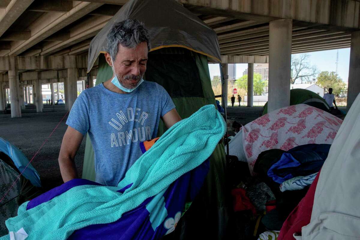 Noel Garza is overcome with emotion as he picks up a blanket that belonged to his friend Delia Kline who died in her sleep overnight. Garza and Kline both lived in a tent under the I-37 overpass.