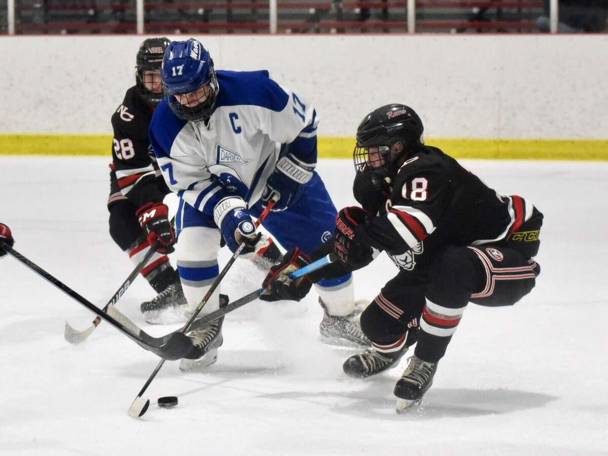 Darien’s Jamison Moore (17) and New Canaan’s Gavin Reid (18) battle for the puck during the FCIAC boys ice hockey semifinals at the Darien Ice House on Thursday.