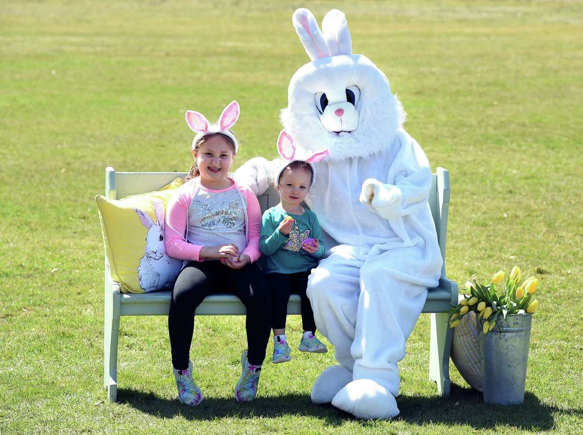 From left, Riley Saxton, 7, and her sister, Quinn, 2, of Milford pose with the Easter Bunny while having their photo taken by Ioescu Smith, owner of AG Productions, at Wasson Field in Milford during the Milford Downtown Business Alliance Easter Eggstravaganza on March 27, 2021.