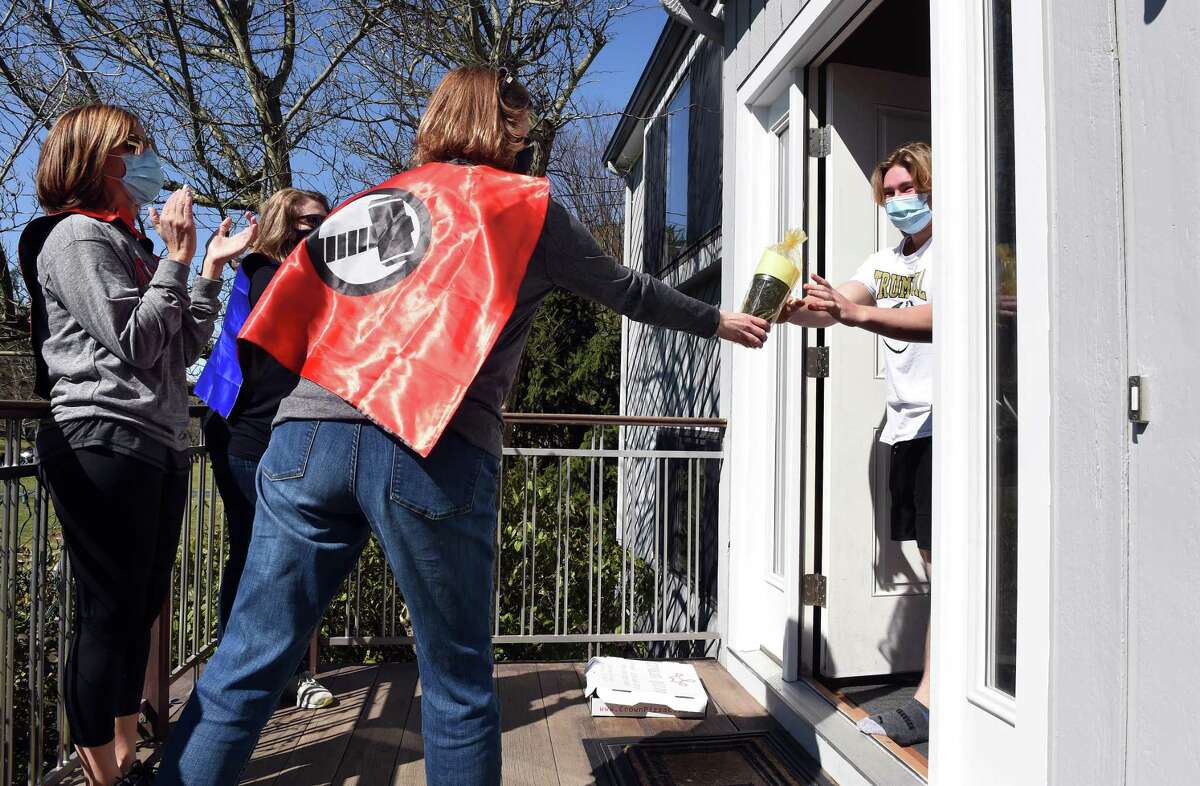 Kristen Kraus, center, along with other Trumbull High School parent volunteers delivers a cup filled with gift cards and treats to graduating senior Jason Knapp at his home in Trumbull on Saturday.