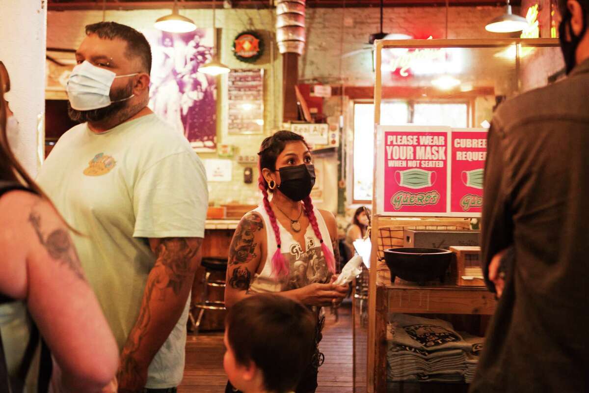 Customers and employees wear masks at a taco bar in Austin, which is still requiring the face coverings in defiance of Gov. Greg Abbott, whose relaxed COVID-19 policies have put Latinos in key industries at greater risk.