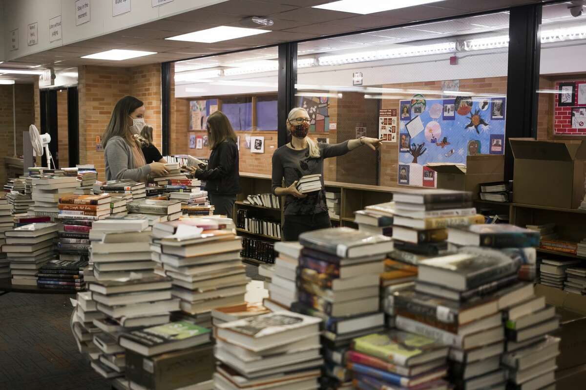 Miriam Andrus, Director of the Grace A. Dow Memorial Library, left, and volunteer Stephanie Williams, right, work with others to organize boxes of books donated by the Salem South Lyon District Library inside the library at Windover High School, which was severely damaged in last year's flood, Wednesday, March 24, 2021. (Katy Kildee/kkildee@mdn.net)