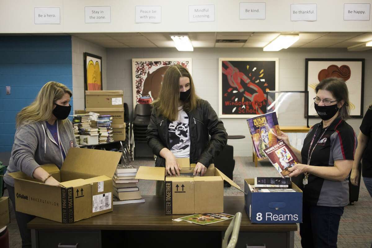 On March 24, Tracy Robinson of the Salem South Lyon District Library, left, her daughter Cailyn, center, and Sally Billotti, a tutor at Windover High School, right, organize boxes of books donated by the Salem South Lyon District Library inside the library at Windover High School, which was severely damaged in last year's flood. (Katy Kildee/kkildee@mdn.net)