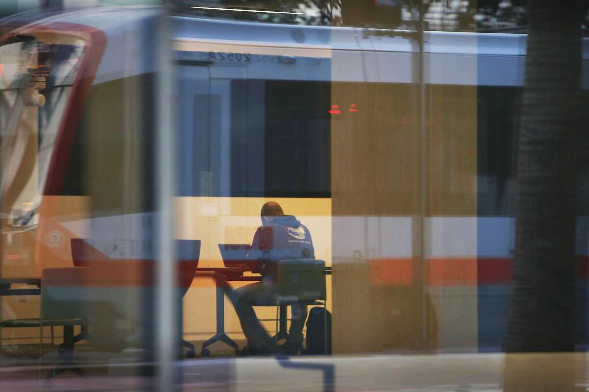 A person is seen working at a table at 1515 Third Street as a street car passing on Third Street is reflected on the exterior of the building at 1515 Third Street on Monday, March 29, 2021 in San Francisco, Calif.