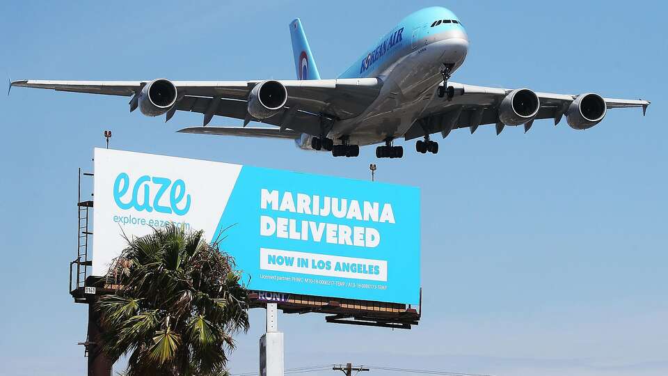 LOS ANGELES, CA - JULY 12: An airplane descends to land at Los Angeles International Airport above a billboard advertising the marijuana delivery service Eaze on July 12, 2018 in Los Angeles, California. A number of marijuana delivery apps are available