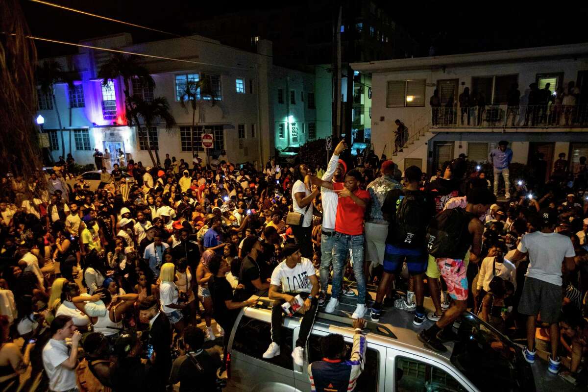 Crowds defiantly gather in the street while a speaker blasts music an hour past curfew in Miami Beach, Florida, on Sunday, March 21, 2021. An 8 p.m. curfew has been extended in Miami Beach after law enforcement worked to contain unruly crowds of spring break tourists.
